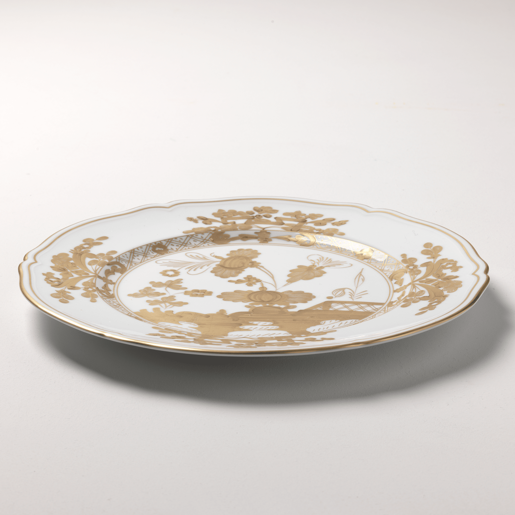 Elevate your dining experience with the exquisite Oriente Italiano Collection Porcelain AURUM Charger Plate, a masterpiece from Ginori 1735. This luxurious charger plate is meticulously crafted from fine white porcelain, offering a canvas for intricate artistry. The delicate floral ornamentation, hand-painted in pure gold, traces the classic lines of the Antico Doccia pattern, a signature of the esteemed Florentine Maison.