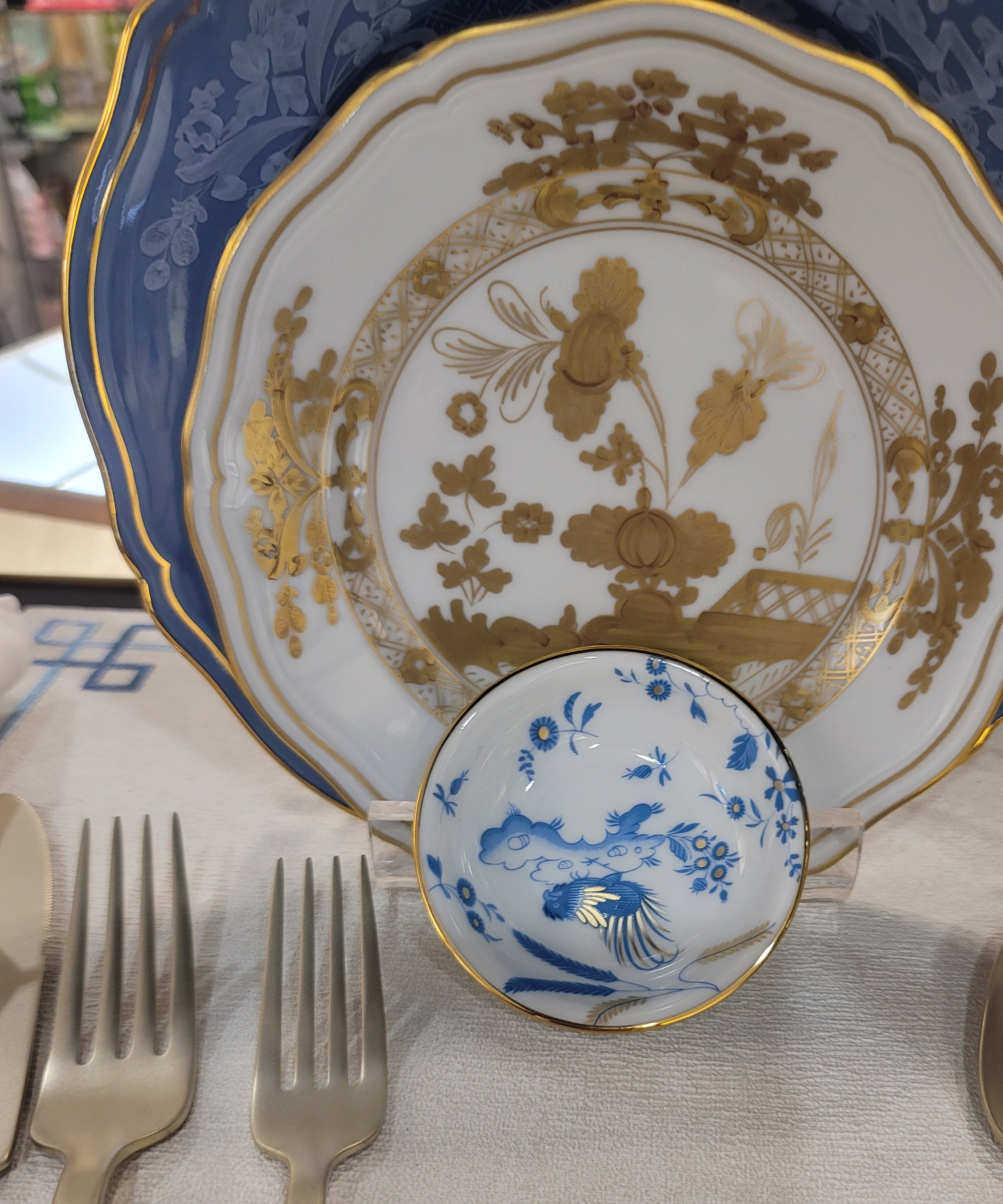 Soy Cup, Dining table setting with decorative plates, spoons, and forks on a white napkin.