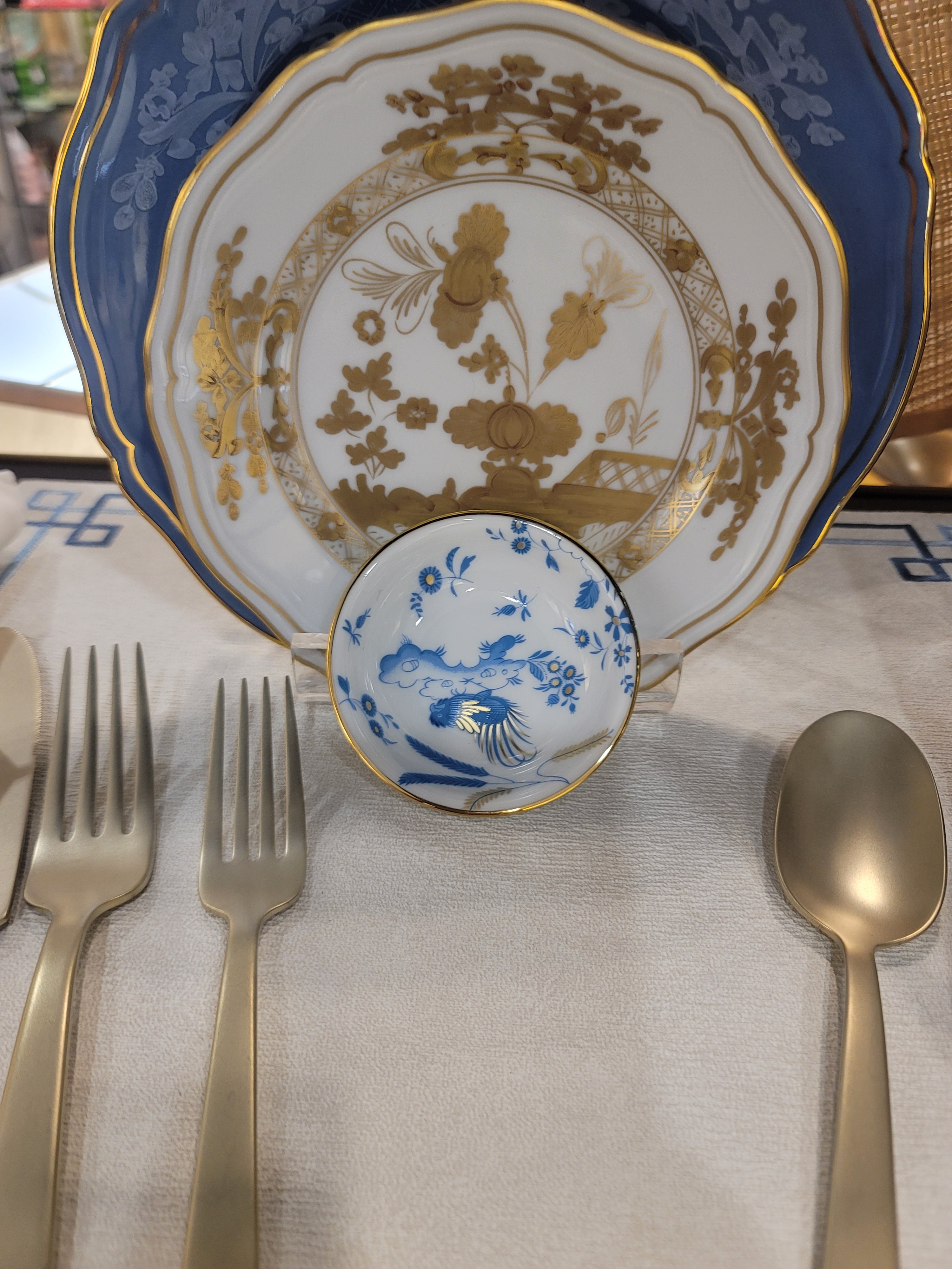 Soy Cup, Dining table setting with decorative plates, spoons, and forks on a white napkin.