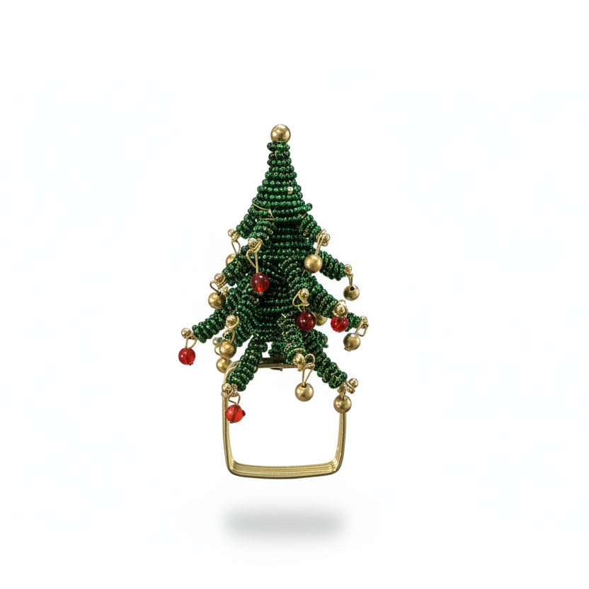 A hand holding a small green beaded Christmas tree ornament with gold and red accents, set against a background of a dark wooden dresser and gray floor.