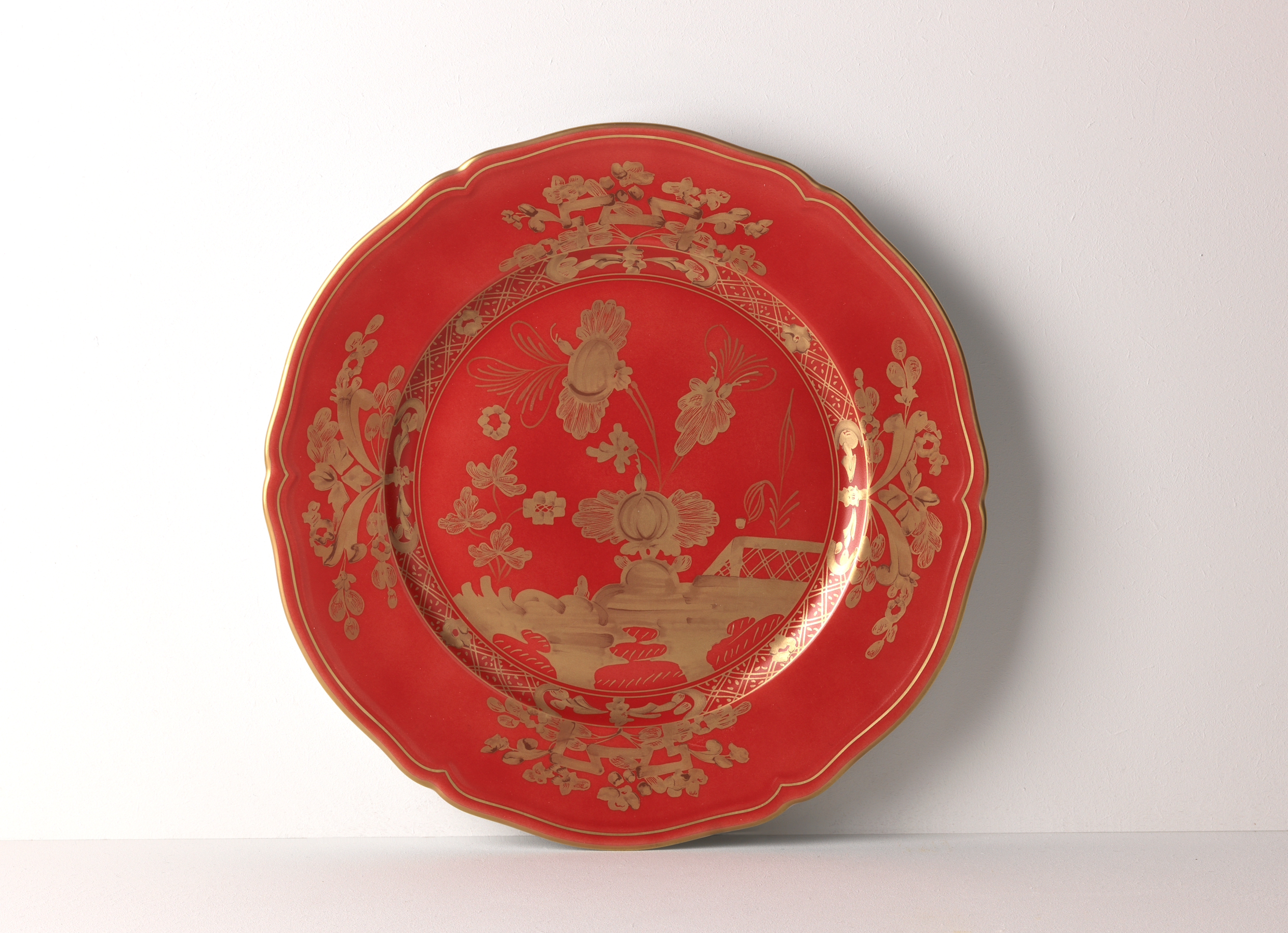 Elevate your dining experience with the exquisite Oriente Italiano Collection Porcelain  RUBRUM Charger Plate, a masterpiece from Ginori 1735. This luxurious charger plate is meticulously crafted from fine white porcelain, offering a canvas for intricate artistry. The delicate floral ornamentation, hand-painted in pure gold, traces the classic lines of the Antico Doccia pattern, a signature of the esteemed Florentine Maison.