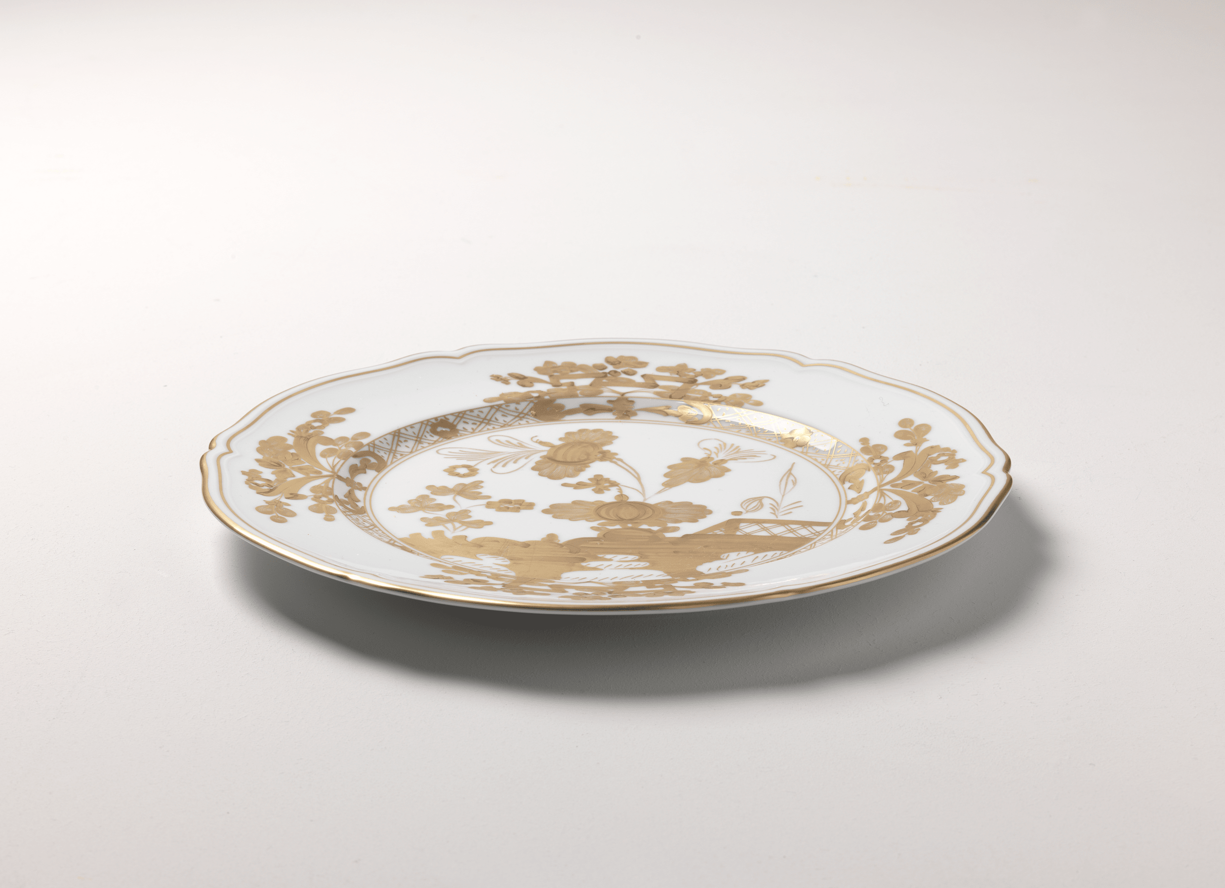 Elevate your dining experience with the exquisite Oriente Italiano Collection Porcelain  AURUM Charger Plate, a masterpiece from Ginori 1735. This luxurious charger plate is meticulously crafted from fine white porcelain, offering a canvas for intricate artistry. The delicate floral ornamentation, hand-painted in pure gold, traces the classic lines of the Antico Doccia pattern, a signature of the esteemed Florentine Maison.